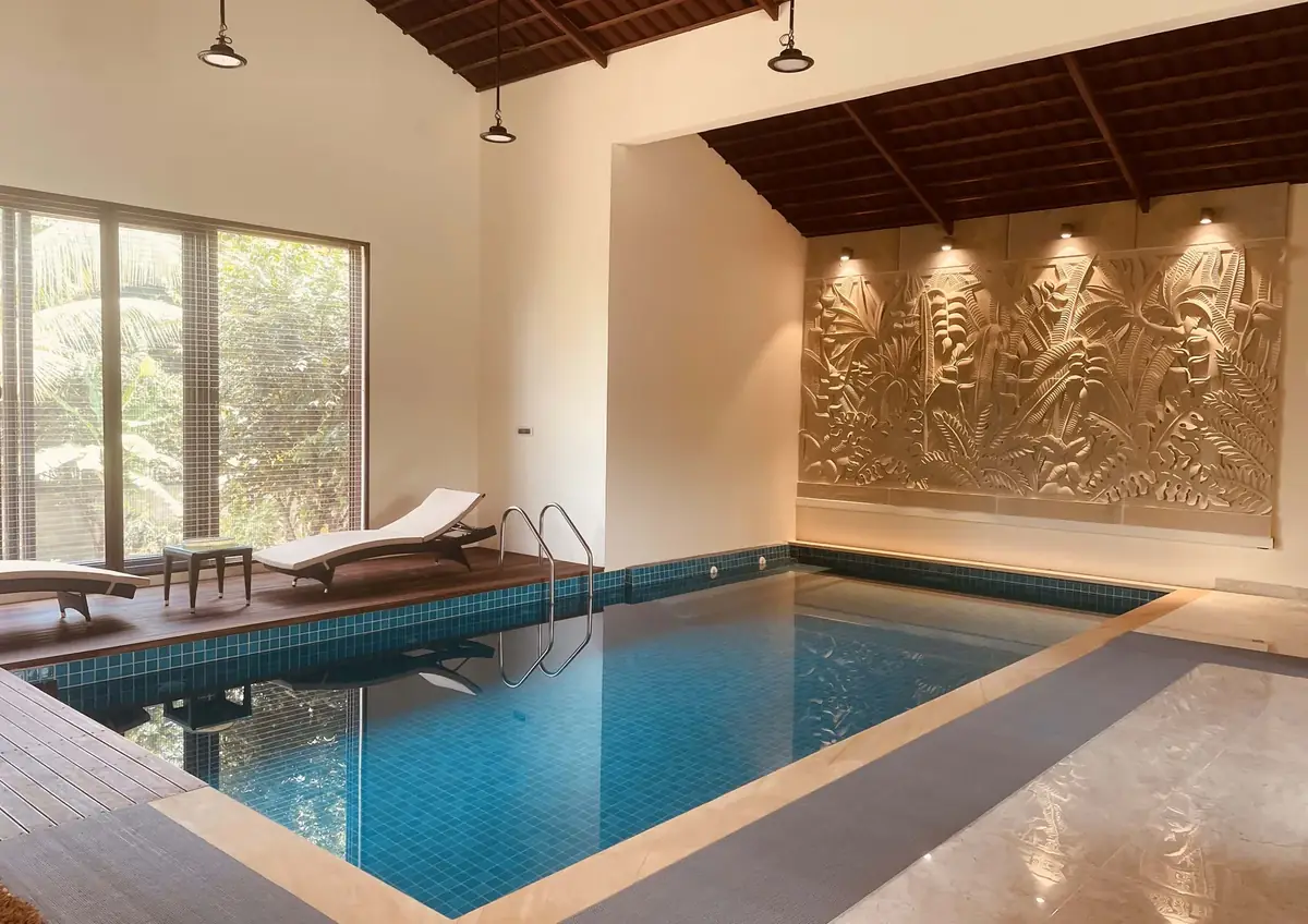 Indoor pool with teak deck and carved stone relief at Sanjeev Residence, Bangalore